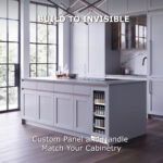A built-in beverage cooler seamlessly integrated into a white kitchen island, showing custom panel and handle matching the surrounding cabinetry with text reading "Build to Invisible."
