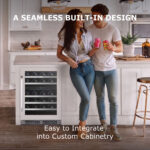A smiling couple holding canned beverages in a contemporary kitchen with an under-counter wine cooler seamlessly installed into the white kitchen island